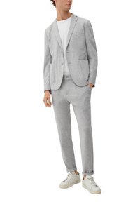 Grijze stretch blazer met twee voorzakken, gecombineerd met bijpassende taps toelopende joggingbroek, gedragen over een wit T-shirt en witte sneakers.