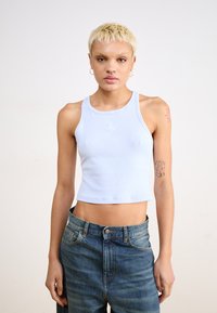 Top corto a coste blu chiaro con scollatura tonda e design senza maniche, caratterizzato da un piccolo logo bianco sul petto. Abbinato a jeans di denim.
