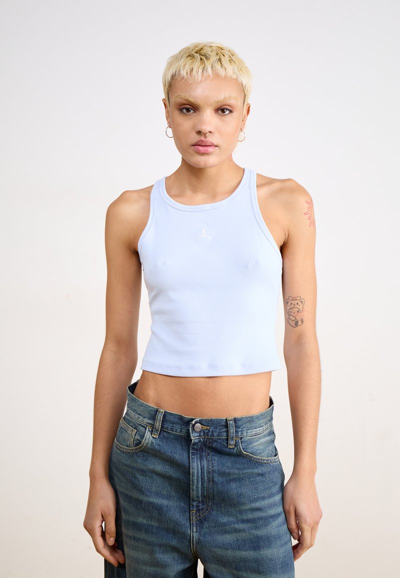 Top corto a coste blu chiaro con scollatura tonda e design senza maniche, caratterizzato da un piccolo logo bianco sul petto. Abbinato a jeans di denim.