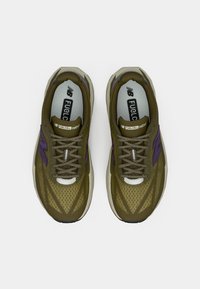 A New Balance FuelCell Rebel sneaker zöld hálós felsőrésszel, lila részletekkel, textúrált dizájnnal és fényvisszaverő fűzőkkel rendelkezik.