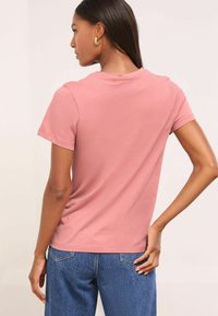 Camiseta de manga corta rosa con un cuello redondo clásico, hecha de algodón suave, de corte ajustado, combinada con vaqueros de denim azul de cintura alta.