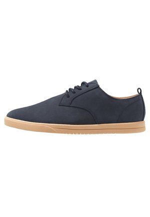 Marineblauwe casual veterschoen met beige rubberen zool en treklus bij de hiel, zijaanzicht op een witte achtergrond.