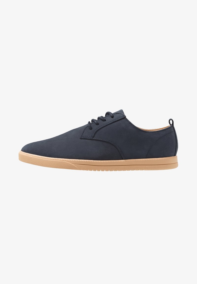 Chaussure décontractée bleu marine à lacets avec semelle en caoutchouc beige et languette arrière, vue de profil sur fond blanc.
