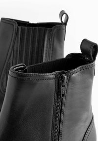 Stivali alla caviglia in pelle nera con chiusure a zip laterali, pannelli elastici e linguette. Texture liscia con dettagli di cucitura meticolosi.