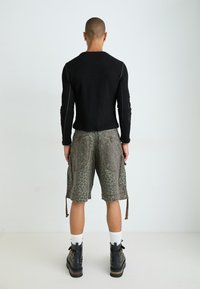 Schwarzes Langarmoberteil mit geripptem Muster, kombiniert mit grauen Cargo-Shorts im Leopardenmuster, die Taschen und einen verstellbaren Saum haben, getragen mit schwarzen Stiefeln.