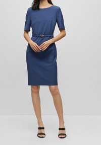 Robe bleu marine jusqu'aux genoux avec manches courtes, tissu texturé, coupe droite et ceinture décorative avec boucle dorée.