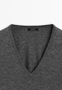 Grijze V-hals trui met een gebreide textuur en een label met de tekst "Massimo Dutti" op de halslijn. Minimalistisch ontwerp op een witte achtergrond.