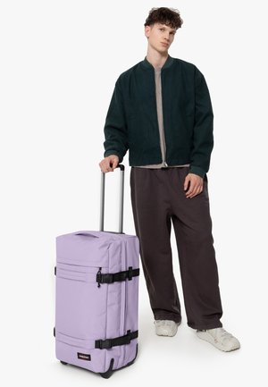 Rolling suitcase in lavender fabric with black accents, multiple compartments, sturdy handles, and a retractable metal handle.