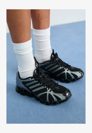 Pantofi sport negri cu accente gri și panouri din plasă, având o talpă texturată și șireturi negre, asortați cu șosete albe cu dungi.