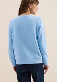 Sweat-shirt bleu clair avec des manches longues et un col rond. Tissu doux, poignets et ourlet côtelés, design simple sans motifs.