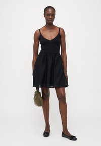 Vestido negro con un corsé ajustado y una falda acampanada. Posee tirantes tipo espagueti, parte superior texturizada y una tela suave y ligera. Se lleva con zapatos planos negros.
