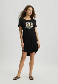 Czarna bawełniana sukienka t-shirt z okrągłym dekoltem, krótkimi rękawami i asymetrycznym dołem. Posiada kolorową grafikę "Beach Vibes".