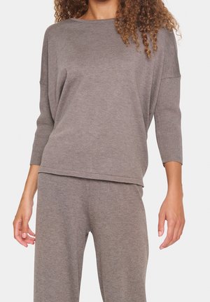 Femme portant un haut en maille ample taupe assorti avec manches trois-quarts et pantalon à jambes larges sur fond uni.