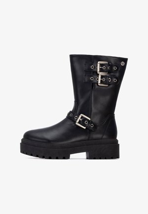 Botas de cuero negras hasta el tobillo con dos acentos de hebilla plateada, suela de plataforma gruesa y un acabado suave; cuenta con una textura de goma negra en la suela.