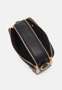 Czarna skórzana torba o teksturowanym wykończeniu, z dwoma złotymi suwakami i złotym akcentem metalowym. Duża przestrzeń wewnętrzna, bez widocznych wzorów.