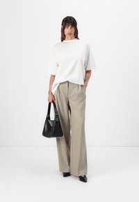 Witte oversized korte mouwen t-shirt, lichtgrijze hoge taille wijde broek, en een zwarte schoudertas met handvat. Soepele stoftexturen.