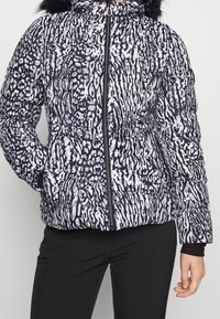 Doudoune à motif abstrait noir et blanc, dotée d'une fermeture éclair frontale, de poches latérales et d'une capuche bordée de fausse fourrure. Tissu texturé.