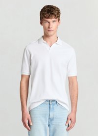 Polo blanc en tissu texturé, avec un col et des manches courtes, associé à un jean bleu clair. Design simple et couleur neutre.