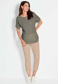 Olivgrünes Strickoberteil mit kurzen Ärmeln, rundem Ausschnitt und strukturiertem Muster. Kombiniert mit beigefarbenen, cropped Hosen und weißen Sneakers.