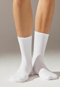 Chaussettes blanches en coton côtelé avec un bord confortable et une texture lisse, ajustées aux chevilles et aux orteils, présentées sur un fond neutre.