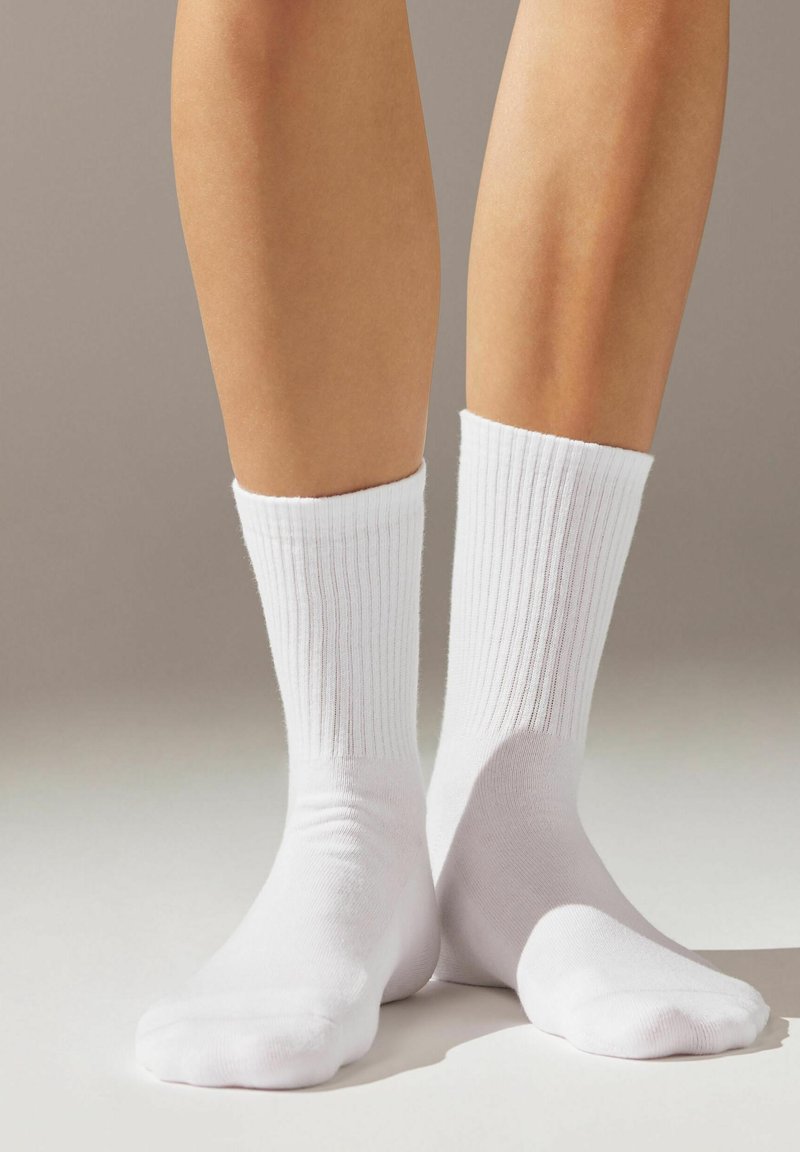 Chaussettes blanches en coton côtelé avec un bord confortable et une texture lisse, ajustées aux chevilles et aux orteils, présentées sur un fond neutre.