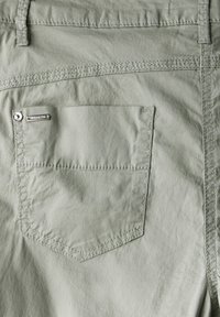 Tylny kieszeń jasnoszarych spodni z widocznym szwem, pętlą na pasek i małą metalową metką z napisem "Street One" w pobliżu górnej krawędzi kieszeni.