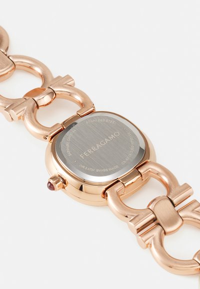 Rose gold stainless steel watch with a square face, link band, and engraved back. Features a red accent on the crown and textured dial.