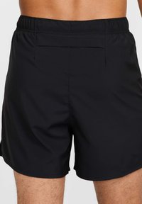 Bañador negro hecho de tela ligera, con una cinturilla elástica y un bolsillo trasero con tapa. Textura suave y corte ajustado.