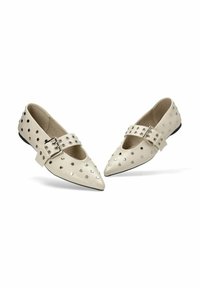 Zapatos planos de punta afilada en cuero crema, con tachuelas metálicas y una sola correa con hebilla a lo largo del empeine. Suela plana negra.