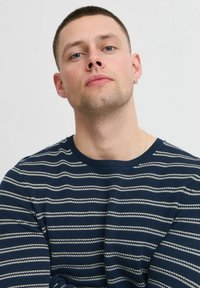 Maglione a righe navy con strisce bianche orizzontali, scollo rotondo e tessuto texture; presenta dettagli di design minimi.