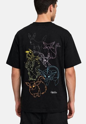Uomo che indossa una maglietta nera con disegni colorati contornati di otto diversi personaggi Pokémon sulla schiena.