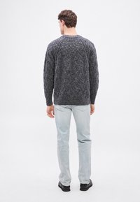 Pelēks džemperis ar kabeles rakstu, apaļu kakla izgriezumu, teksturētu rakstu un ribotām aprocēm, kopā ar gaiši zilām džinsa biksēm un melniem apaviem.