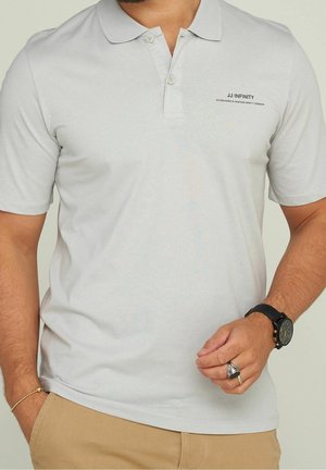 Jasnoszara koszulka polo wykonana z gładkiej tkaniny. Posiada klasyczny kołnierzyk, listwę na dwa guziki oraz logo na piersi.