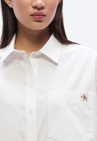 Λευκό πουκάμισο με κουμπιά από απαλό ύφασμα, με γιακά και αριστερή τσέπη στο στήθος με μικρό λο γότυπο Calvin Klein.