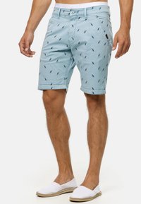 Light blue cotton shorts featuring a small bird pattern, front pockets, and rolled hems. Paired with white slip-on shoes.