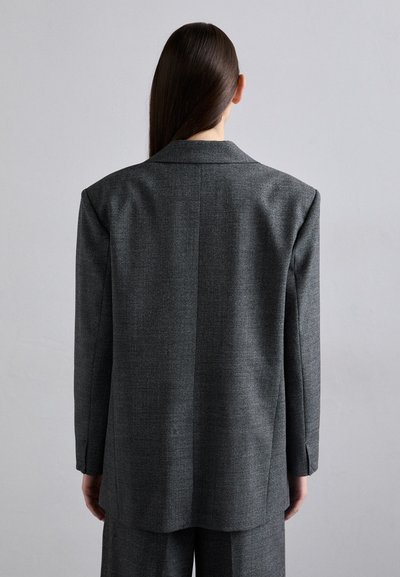 Grå struktureret blazer med en tekstureret overflade, brede revers og standard pasform. Har en midtersøm på ryggen og lange ærmer.