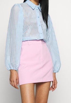 Žena nosící světle modrou průhlednou kostkovanou blůzu s dlouhými nafouklými rukávy zastrčenou do vysoké pastelově růžové mini sukně.