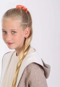 Hellbrauner Kapuzenpullover mit cremefarbenen Akzenten, kombiniert mit einem lebhaften orangefarbenen Satin-Haargummi in geflochtenem blonden Haar.