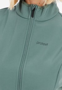 Jasnozielona kurtka na zamek z wysokim kołnierzem, o gładkiej fakturze, z logo marki "protest" wydrukowanym na czarno.