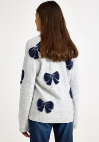 Pulover gri deschis cu modele de fundițe albastru închis. Are guler rotund, manșete și tiv cu dungi. Textură moale, croială casual.