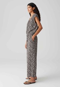 Tuta a righe in bianco e nero con maniche ampie, scollatura a V, vita aderente e tasche laterali, abbinata a sandali neri piatti.