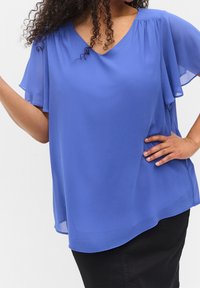Top en chiffon bleu avec un décolleté en V et de courtes manches volantées, offrant une coupe ample et un ourlet arrondi, associé à un bas noir.