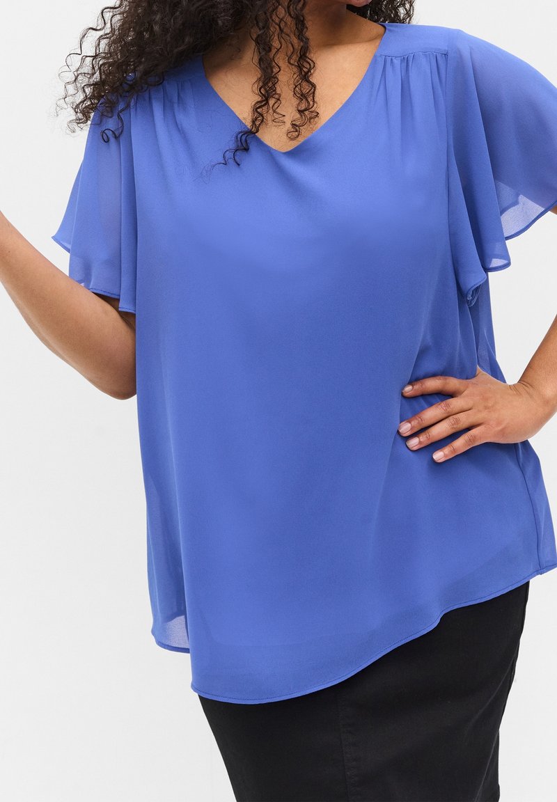 Top en chiffon bleu avec un décolleté en V et de courtes manches volantées, offrant une coupe ample et un ourlet arrondi, associé à un bas noir.