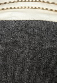 Tmavě šedá pletená tkanina s měkkou texturou a hustým vazem, doplněná kontrastní světlou látkou a kovovým zipem podél horní části.