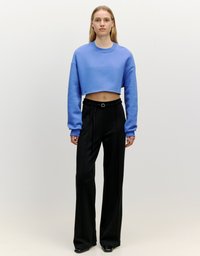Gekürzter blauer Sweatshirt mit langen Ärmeln, kombiniert mit hoch taillierten schwarzen Hosen. Das Outfit verfügt über einen Gürtel und schicke, glänzende schwarze Schuhe.