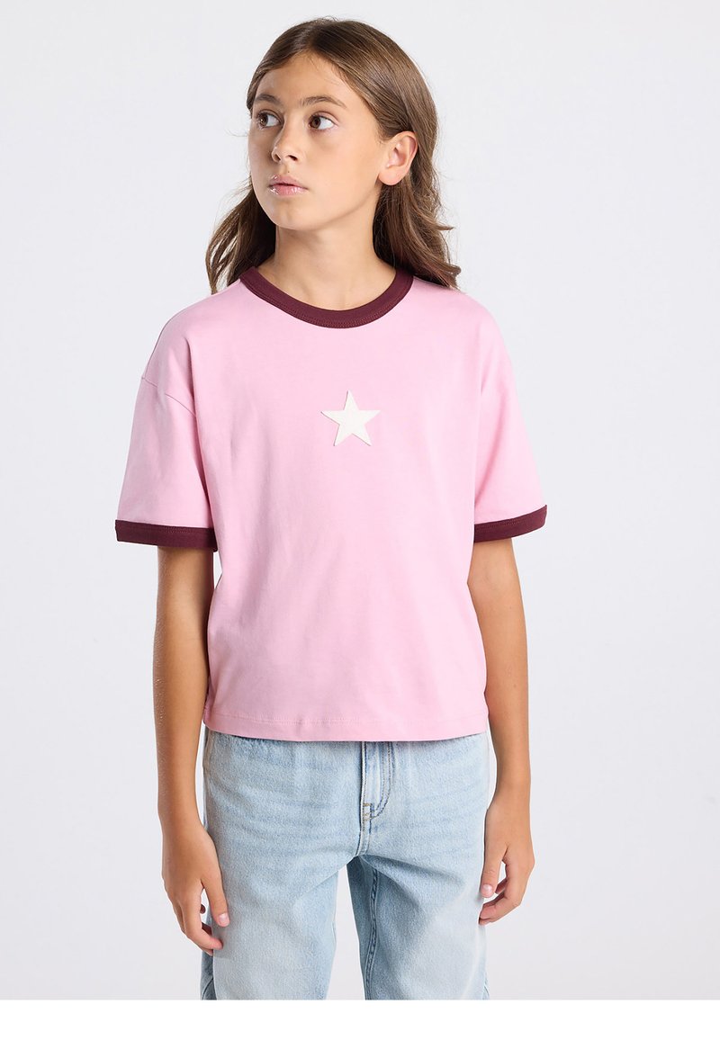 T-shirt rose à manches courtes avec un col et des poignets ronds bordeaux, arborant un motif d'étoile blanche sur le devant. Coupe décontractée.