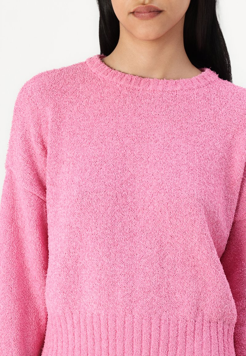 Flauschiger pinkfarbener Pullover mit geripptem Saum und Ausschnitt; bietet eine lockere Passform und eine strukturierte Oberfläche. Das weiche Material sorgt für ein gemütliches Erscheinungsbild.
