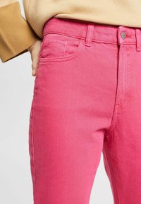 Jeans de mezclilla rosa con un diseño ajustado, estilo de cinco bolsillos y detalles de costura. La tela parece suave con una textura ligeramente desgastada.