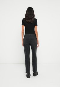 Čierny top s krátkym rukávom v kombinácii s tmavými džínami s vysokým pásom. Džínsy majú rovný strih nohavíc a dve zadné vrecká, ktoré vytvárajú čistú siluetu.