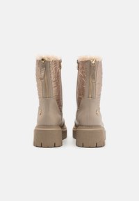 Beige ankel støvler med quiltet design, teksturert stoff, sidesyninger og imitasjonspelskant på toppen. Tykk gummisåler med ribber.